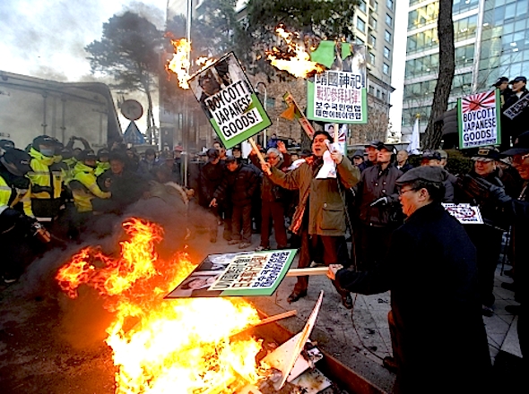 South Korean protesters burn a effigy of Japanese Prime Minister Shinzo Abe, banners and Japanese flag as police officers spray fire extinguishers during a rally denouncing about Japanese Prime Minister Shinzo Abe in front of the Japanese Embassy in Seoul, South Korea, Friday, Dec. 27, 2013. Prime Minister Shinzo Abe paid his respects at a shrine honoring Japan's war dead in an unexpected visit Thursday that drew sharp rebukes from China and South Korea, who warned that the move celebrates his country's militaristic past and could further sour relations. (AP Photo/Lee Jin-man)